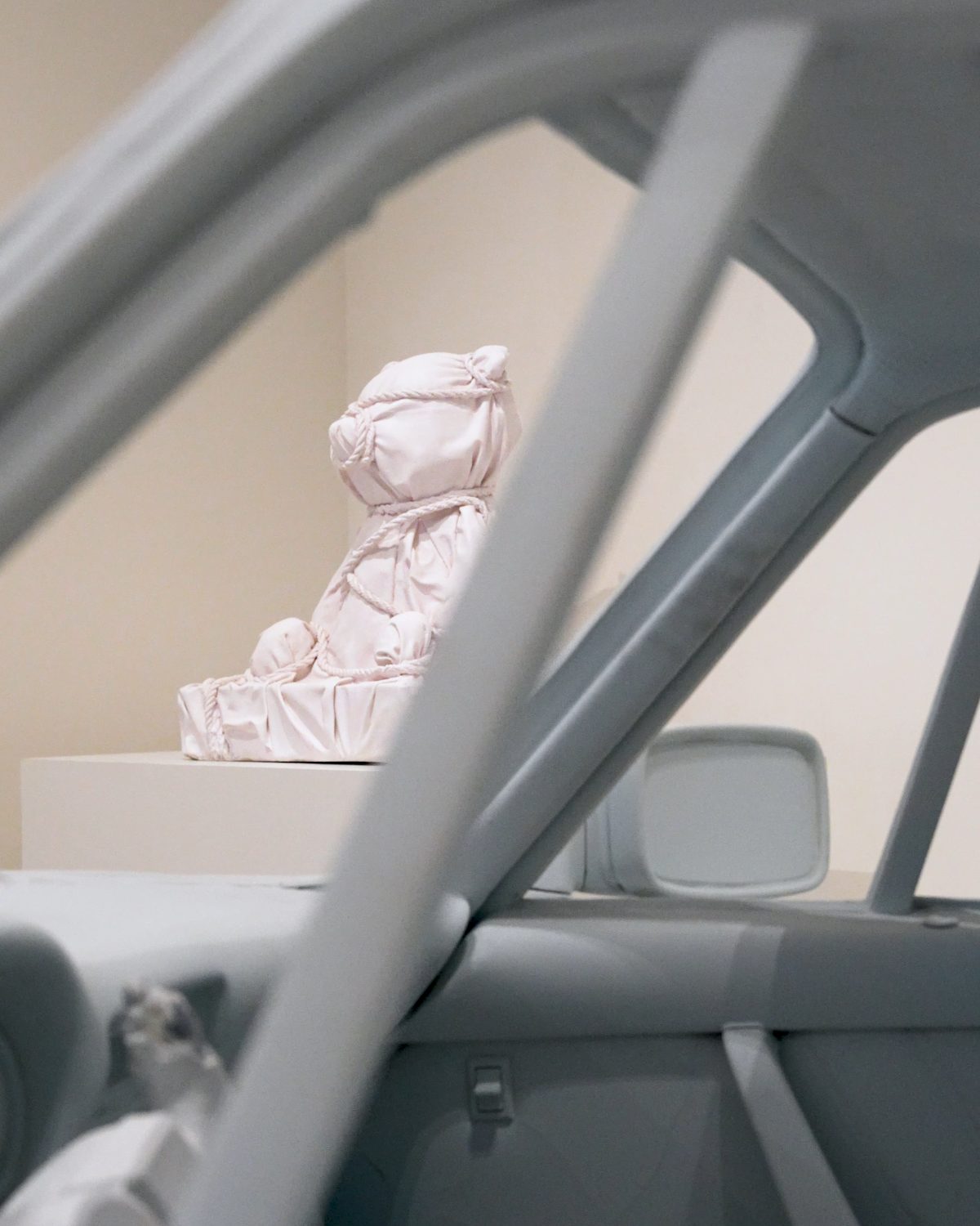a wrapped pink teddy sculpture seen through a car window