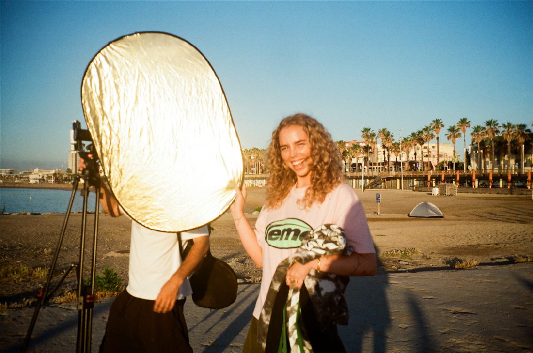 Two of the crew on the beach, one holding a gold reflector into the low sun