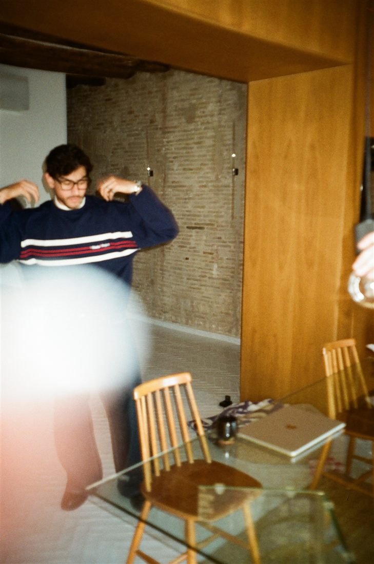 Pulling on a striped sweater indoors, a light leak across the frame
